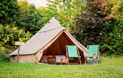 A cozy teepee tent with two green chairs and a lantern in front, set in lush nature at RØSTIG Dorst, Netherlands.