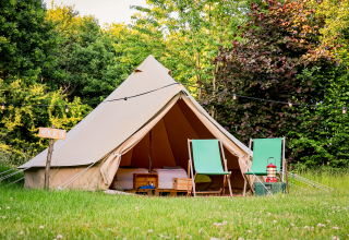A cozy teepee tent with two green chairs and a lantern in front, set in lush nature at RØSTIG Dorst, Netherlands.