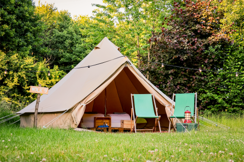 A cozy teepee tent with two green chairs and a lantern in front, set in lush nature at RØSTIG Dorst, Netherlands.