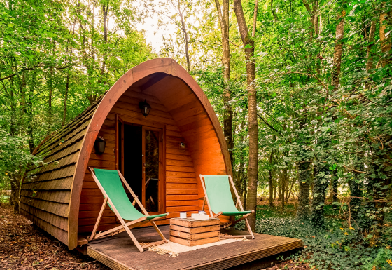 Cabaña Duo Pod Large en RØSTIG Dorst, Países Bajos, rodeada de bosque y dos sillas verdes al frente.