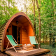 Duo Pod Large Holzhütte bei RØSTIG Dorst, Niederlande, im Wald mit zwei grünen Stühlen davor.