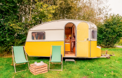 Retro gul campingvogn med åbne døre, to stole og et bord på græsplæne ved RØSTIG Dorst, Holland.