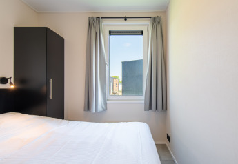 Chambre au Wood Lodge avec lit simple, armoire noire et fenêtre avec rideaux gris à Kompas Camping Nieuwpoort.