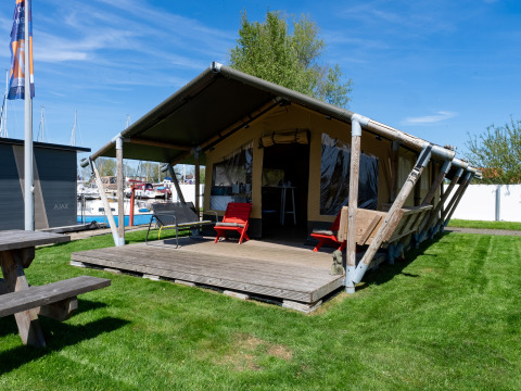 Safaritent Heeg op Marina Heeg in Nederland, met houten veranda, grasveld en zicht op boten.
