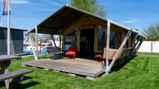 Safaritent Heeg op Marina Heeg in Nederland, met houten veranda, grasveld en zicht op boten.