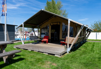 Tente safari Heeg à la Marina Heeg aux Pays-Bas, terrasse en bois, pelouse et bateaux proches.