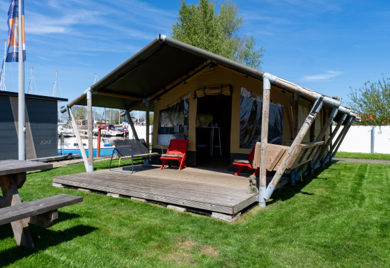 Tente safari Heeg à la Marina Heeg aux Pays-Bas, terrasse en bois, pelouse et bateaux proches.