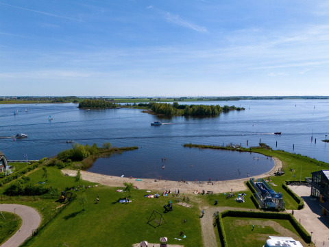 Vista de la playa y el lago en Marina Heeg en Países Bajos, con áreas verdes y personas disfrutando.