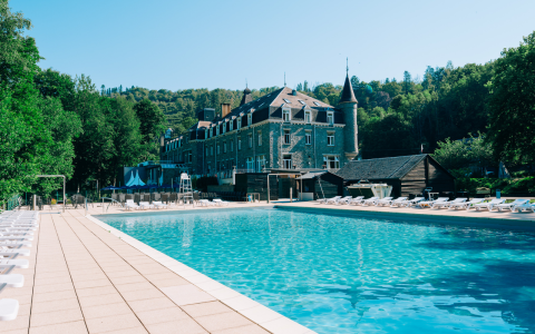 Großer Außenpool mit Liegestühlen vor einer glamping Unterkunft im Schlossstil, umgeben von grünen Bäumen.