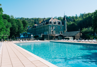 Großer Außenpool mit Liegestühlen vor einer glamping Unterkunft im Schlossstil, umgeben von grünen Bäumen.