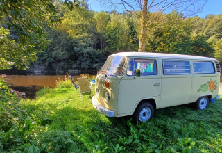 Campervan d'epoca parcheggiato vicino al fiume al Camping Floreal La Roche-en-Ardenne, Belgio, immerso nel verde.