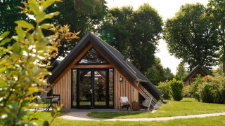 Tiny house Wellness Lodge en bois avec terrasse à l'avant, chaises longues et cadre verdoyant.