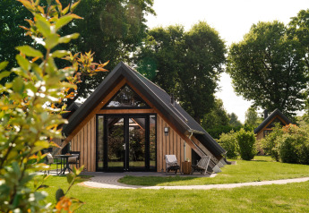 Tiny House namens Wellness Lodge mit Veranda, Gartenmöbeln und viel Grün im Hintergrund.