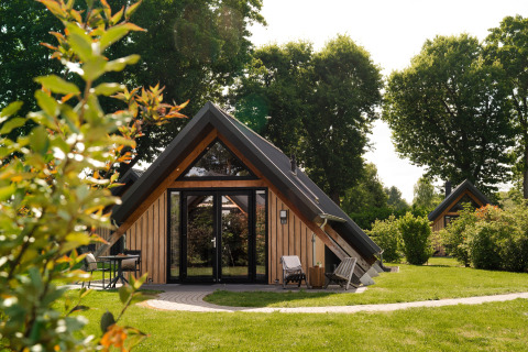 Houten tiny house genaamd Wellness Lodge met terras, grasveld en veel bomen op de achtergrond.