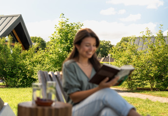 Mujer leyendo un libro al aire libre en la Wellness Lodge de Holiday Park De IJsvogel, Países Bajos, día soleado.
