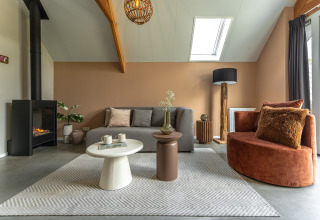 Moderne woonkamer met haard, grijze bank en warme accenten in Wellness Lodge, De IJsvogel, Nederland.