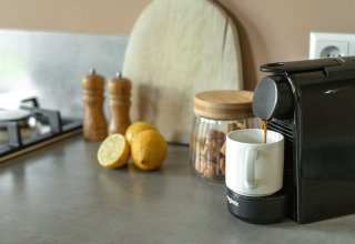 Cafetera preparando café en una taza sobre la encimera con limones, galletas y molinillos de especias.