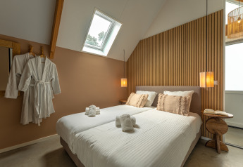 Dormitorio moderno en Wellness Lodge, Holiday Park De IJsvogel, Países Bajos, con cama doble y albornoces.