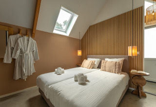 Moderne slaapkamer in Wellness Lodge, Holiday Park De IJsvogel, Nederland, met tweepersoonsbed en badjassen.