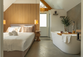 Lyst og moderne værelse i Wellness Lodge med dobbeltseng og fritstående badekar på Holiday Park De IJsvogel.