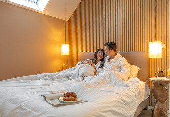 Pareja con albornoces desayunando en la cama en Wellness Lodge, Holiday Park De IJsvogel, Países Bajos.