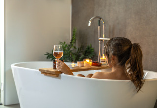 Mujer relajándose con una copa de vino en la bañera en Wellness Lodge, Holiday Park De IJsvogel, Países Bajos.