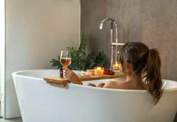 Mujer relajándose con una copa de vino en la bañera en Wellness Lodge, Holiday Park De IJsvogel, Países Bajos.