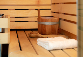Innenraum einer Sauna mit Holzbank, Wassereimer, Kelle und Handtuch im Wellness Lodge, Niederlande.