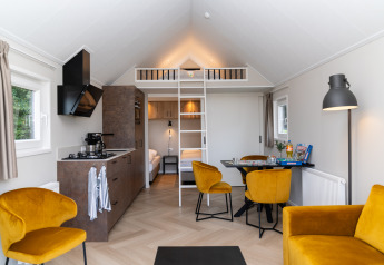 Modern lodge interior with yellow chairs, kitchenette, and loft at Berg Lodge - Sauna, Resort Mooi Bemelen, NL.
