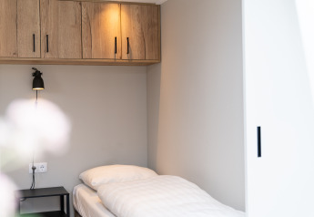 Chambre simple minimaliste avec literie blanche, lampe murale et placards bois au Berg Lodge - Sauna, Resort Mooi Bemelen.