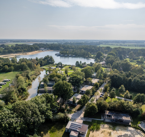 Vista aérea de un alojamiento glamping junto al lago, rodeado de zonas verdes y árboles en un día soleado.
