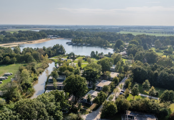 Vista aérea de un alojamiento glamping junto al lago, rodeado de zonas verdes y árboles en un día soleado.