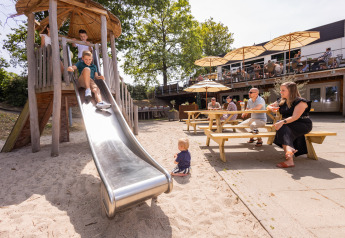 Des enfants jouent sur un toboggan pendant que des adultes se détendent à des tables dans un glamping.