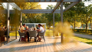 Une famille partage un repas en plein air sur une terrasse en bois d’un logement glamping entouré d’arbres.