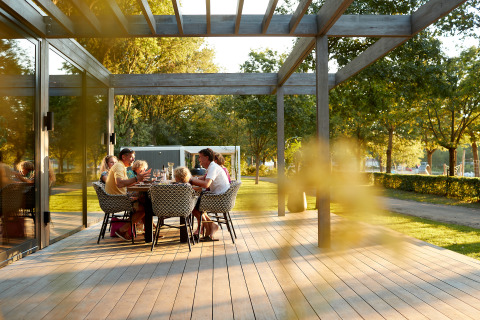 Una familia comparte una comida al aire libre en una terraza de madera en un alojamiento glamping rodeado de árboles.