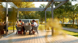 Une famille partage un repas en plein air sur une terrasse en bois d’un logement glamping entouré d’arbres.