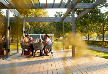 Una famiglia fa un pasto all’aperto sul terrazzo di legno di un alloggio glamping circondato da alberi.