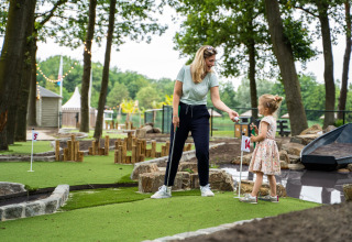 Une mère et sa fille jouent au mini-golf dans un hébergement glamping en plein air entouré d'arbres.