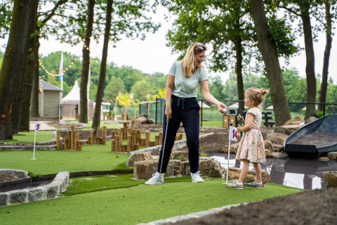 Mama en dochter genieten samen van minigolf op een glampingverblijf tussen de bomen.