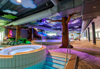 Espace piscine intérieure dans un hébergement glamping avec jacuzzi, arbres artificiels et décor ludique.