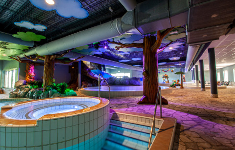 Zona de piscina interior en alojamiento glamping con jacuzzi, árboles artificiales y decoración colorida.