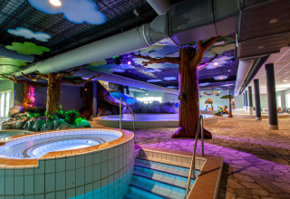 Zona de piscina interior en alojamiento glamping con jacuzzi, árboles artificiales y decoración colorida.