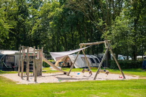 Parque infantil con columpios y tobogán en un alojamiento glamping rodeado de tiendas y naturaleza.