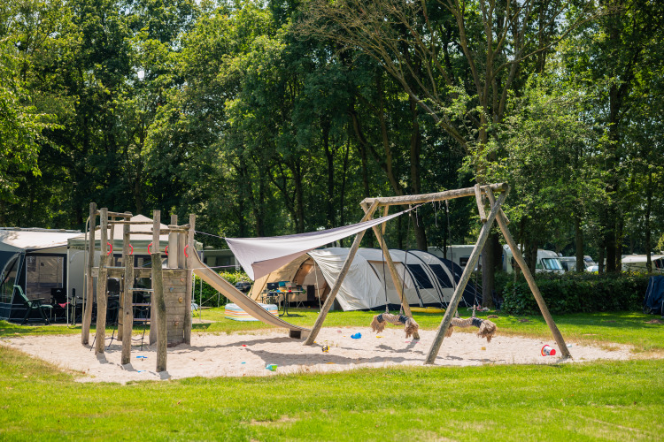Playground with swings and slide at a glamping site featuring tents and lush green surroundings.