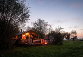 Tenda safari Smûk Tent Huske con veranda e falò a Smûk Recreatie nei Paesi Bassi al tramonto.