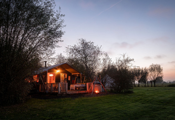 Tenda safari Smûk Tent Huske con veranda e falò a Smûk Recreatie nei Paesi Bassi al tramonto.
