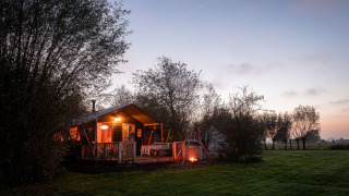 Tienda safari Smûk Tent Huske con porche y fogata en Smûk Recreatie, Países Bajos, al atardecer.