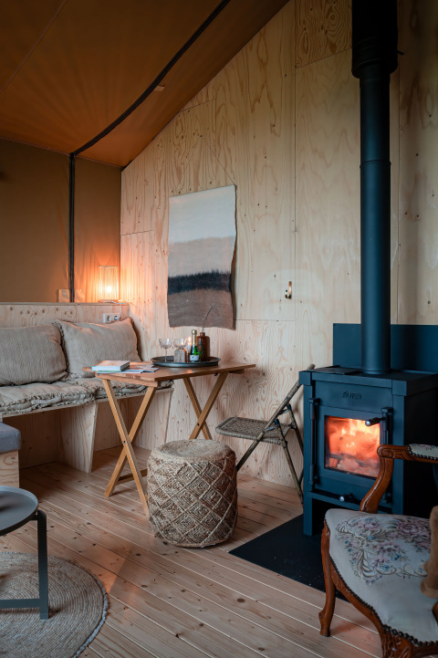 Intérieur chaleureux de la tente safari Smûk Tent Huske, avec poêle à bois, assises et murs en bois.