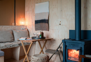 Intérieur chaleureux de la tente safari Smûk Tent Huske, avec poêle à bois, assises et murs en bois.