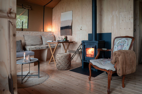 Intérieur chaleureux d'une tente safari avec poêle à bois chez Smûk Tent Huske aux Pays-Bas.